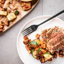Blackened cod with vegetables cooked on a sheet pan and served on a plate with a fork.