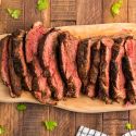 Blackened steak with a charred outside sliced on a wooden cutting board.