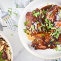 Broiled spicy barbecue chicken thighs on a plate with cilantro and a salad on the side.