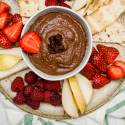 Brownie batter hummus in a bowl with cut fruit and crackers.