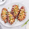 Buffalo chicken stuffed sweet potatoes on a plate with ranch dressing and green onions.