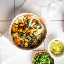 Butternut squash and egg breakfast casserole with turkey sausage in a baking dish with avocado on the side.