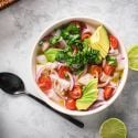 Ceviche with fish marinated in lime juice and served with cilantro, avocado, tomatoes, and red onion in a white bowl.