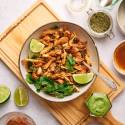 Chicken carnitas in a bowl sitting on a wooden cutting board with ingredients around it. 