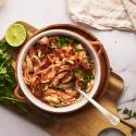 Chicken tinga in a bowl with onions, cilantro, avocado, and queso fresco.