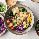 A chicken chipotle ranch bowl topped with creamy ranch sauce, sliced tomatoes, black beans, corn, avocado, red cabbage, and green onions.