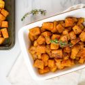 Cinnamon roasted butternut squash in a white dish with a baking sheet. 