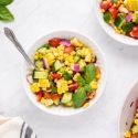 Corm salad with fresh corn, cucumbers, cherry tomatoes, and red onion in a bowl with vinaigrette and basil.