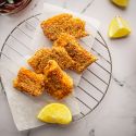 Crispy baked fish with breading on a wire rack with lemons and salad.