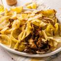 A white plate of roasted cabbage with crispy edges, garnished with lemon wedges. A bottle of olive oil and a wooden pepper mill are in the background.