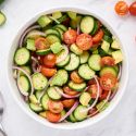 Cucumber salad with tomatoes, avocado, red onion, and vinaigrette in a large bowl.