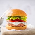 Ground chicken burger with ranch dressing, tomatoes, and lettuce on a burger bun.