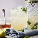 A refreshing drink with mint and ice, next to a jar of honey and lime wedges on a blue napkin.