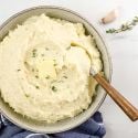 Cauliflower mashed potatoes with roasted garlic and butter in a ceramic bowl with a wooden spoon.