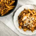 Sausage pasta with cauliflower, garlic, and tomatoes on a plate with Parmesan cheese.