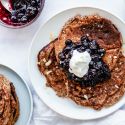 Greek yogurt and flax pancakes on a plate with blueberry compote, whipped cream, and almonds.