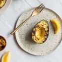 Grilled avocados on a plate with olive oil, lemon, salt, and pepper.