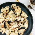 Grilled cauliflower with browned edges on a plate with fresh parsley.