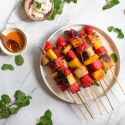 Grilled fruit kabobs with banana, watermelon, strawberries, and mango on wooden skewers with honey and mint.