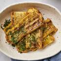 Grilled yellow squash on a black plate sprinkled with parsley.