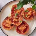 Grilled tomatoes topped with fresh basil, drizzled with olive oil, served on a round plate alongside a bowl of broth.