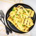 Grilled yellow squash on a black plate sprinkled with parsley.