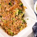 Healthy broccoli casserole with mushrooms, cheddar cheese, and crispy onions in a baking dish with a spoon.