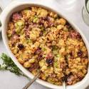 Healthy cornbread stuffing with sausage, celery, and dried cranberries  in baking dish with spoons ready to serve.