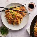 Healthy fried rice with cabbage, carrots, and vegetables served on a plate with chopsticks and in a wok.