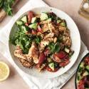 A dish featuring grilled chicken, fresh vegetable salad, lettuce, and grains, topped with fresh mint leaves.