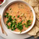 Healthy queso dip with melted cheddar cheese, diced tomatoes, and jalapeños in a bowl with tortilla chips.