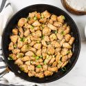 Healthy Sesame Chicken in a skillet with green onions with white rice and broccoli on the side.