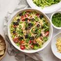 Healthy taco dip with seasoned cream cheese, refried beans, lettuce, salsa, and shredded cheese in a bowl with tortilla chips.