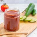 Homemade taco sauce made with tomato sauce, vinegar, spices, and sugar in a glass jar on a cutting board.