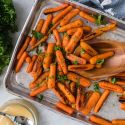 Honey roasted baby carrots with crispy edges on a baking sheet with salt, pepper, honey, and chopped parsley.