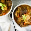 Instant pot beef stew with tender beef, carrots, and potatoes in two bowls with fresh herbs.