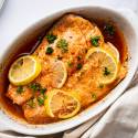 Lemon pepper salmon with slices on lemon and parsley in a white baling dish.