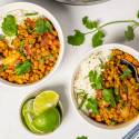 Bowls of lentil coconut curry served over white rice, garnished with fresh cilantro and lime wedges.