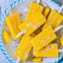 Mango popiscles made with fresh mango pieces, lime juice, water, and honey on a plate with ice.