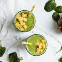 Mango spinach smoothie in two cups with fresh mango chunks on top.