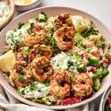 Mediterranean shrimp bowl featuring grilled shrimp, quinoa, chopped vegetables, tzatziki sauce, and lemon wedges, garnished with fresh parsley.