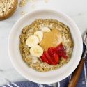 Banana Peanut Butter Microwave Oatmeal in a bowl with rolled oats, bananas, peanut butter, and strawberries.
