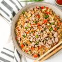 Cauliflower rice with ground pork, cabbage, carrots, and green onion in a bowl with chopsticks.