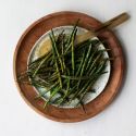 Roasted green beans with olive oil, balsamic vinegar, garlic powder, salt, pepper, and Italian seasoning on a wooden plate with a spoon. 