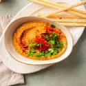 Roasted red pepper hummus made with chickpeas, tahini, garlic, lemon, and olive oil in a bowl with cilantro and paprika.