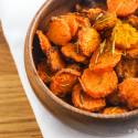 Baked carrot chips in a wooden bowl with rosemary, salt, and pepper.