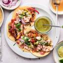 Salmon fajitas with flaked salmon, peppers, onions, cilantro, and green salsa served in corn tortillas.