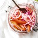Salsa criolla with red onions, tomatoes, and lime juice in a glass jar with a spoon.