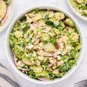 Shaved Brussels sprouts salad with creamy honey dijon dressing, sliced apples, goat cheese, almonds, and red onions in a bowl.