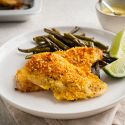 Sheet pan lemon pepper chicken coated with breadcrumbs and Parmesan cheese on a plate with roasted green beans,